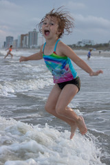 Young girl happy and jumping over ocean wave