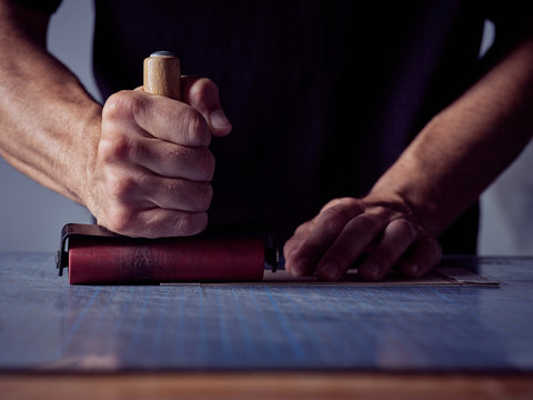 Crop craftsman standing by table with cutting pad and using roller for leather work while making book bind