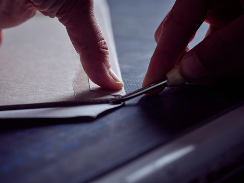 Worker cutting sheet with stationery knife on surface