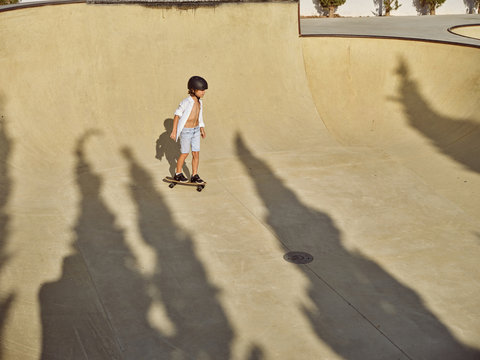 From above happy little boy wearing protective helmet and riding skateboard on ramp in skatepark