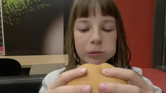 Young happy teenager eating tasty hamburger in fast food restaurant. Teen girl eating french fries for dinner at fast food cafe.