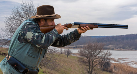 Hunting period, autumn season open. A hunter with a gun in his hands in hunting clothes in the autumn forest in search of a trophy. A man stands with weapons and hunting dogs tracking down the game.	