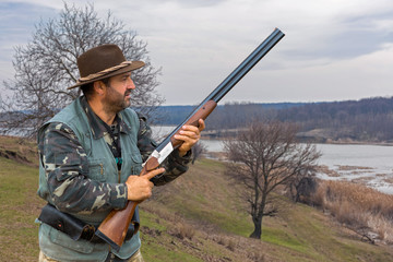 Fototapeta premium Hunting period, autumn season open. A hunter with a gun in his hands in hunting clothes in the autumn forest in search of a trophy. A man stands with weapons and hunting dogs tracking down the game. 