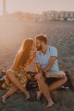 Bearded amorous man and long haired woman eating together pizza in sunlight