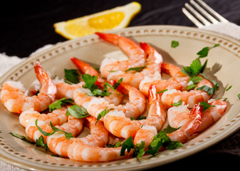 Prawns Shrimps on a plate with lemon, garlic and herbs on black background.