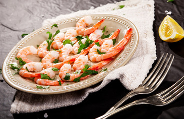 Prawns Shrimps on a plate with lemon, garlic and herbs on black background.