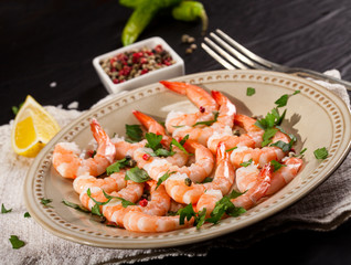Prawns Shrimps on a plate with lemon, garlic and herbs on black background.