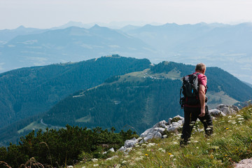 An old man in backpack looks at the alpine mountains. Summer day