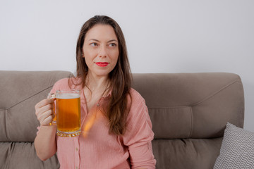 Woman sitting on the couch and holding glass with beer.