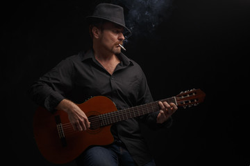 Man in black clothes plays a classic acoustic guitar. Studio photography.