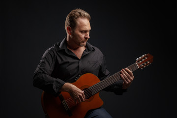 Man in black clothes plays a classic acoustic guitar. Studio photography.