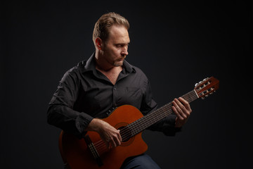 Obraz premium Man in black clothes plays a classic acoustic guitar. Studio photography.