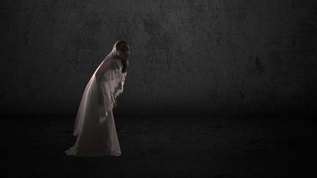Digital composite of scary zombie with wounded face and wearing bride gown walking on dark background. Halloween concept. Shot in 4k resolution