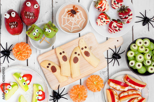 Healthy Halloween fruit snacks. Selection of fun, spooky treats. Top view table scene over a white wood background.