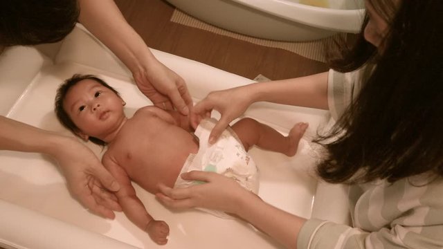 Asian parents changing their baby diaper after bath, at home, child care