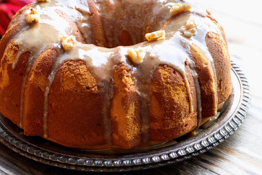 Delicious, Pumpkin Spice Bundt Cake frosted with brown sugar glaze and walnuts oven a rustic wood table background. 