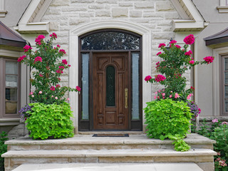 Elegant wooden front door of stone house surrounded by flowers