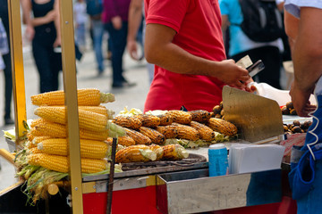Street vendor prepares roasted chestnuts and corn on cobs on his street vendor cart.