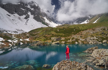 Hiking woman in red jacket stay at beautiful lake in mountains.