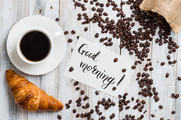 Classic croissant with coffee on a light wooden background with the inscription «good morning» with copy space
