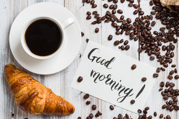 Classic croissant with coffee on a light wooden background with the inscription «good morning» with copy space