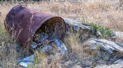 Obraz premium Large rusty iron barrel with plastic trash inside. Garbage in the forest. Environmental pollution by plastic. Bottles, cans in the dry grass. Global problem of Earth. 