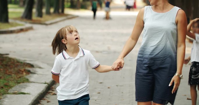 Preteen boy suffering Down syndrome holding mother's hand and walking in park, importance of communication