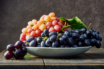 Fresh grapes. Bunches of different varieties in a plate on an old wooden table and dark background. soft focus