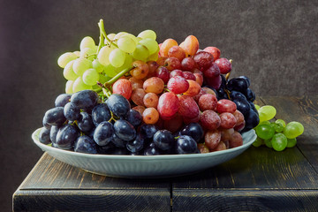 Fresh grapes. Bunches of different varieties in a plate on an old wooden table and dark background. soft focus