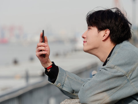 Portrait of a handsome Chinese young man in jeans holding his mobile phone, looking for something interesting in internet, mobile phone and the internet take up a lot of teenager's time.