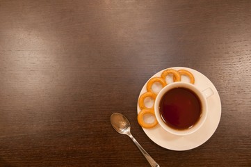 Cup of tea with a spoon, with bagels, on a brown wood table