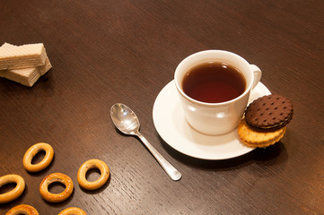 black tea in a white cup on a saucer with a spoon, with cookies and bagels on a dark wooden table