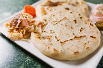 Pupusas served with vegetable garnishes and sauce on square white plate