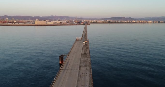 vuelo dron sobre puente pantalan de puerto abandonado en amanecer dorado anaranjado con un mar mediterraneo sereno y solitario
