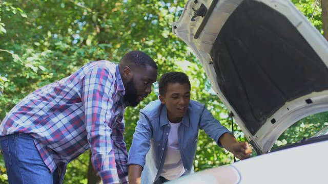 Black dad praising teenage son learning to repair car, family togetherness