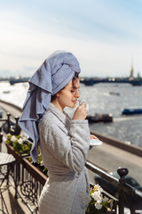 Young beautiful happy woman after a shower in a bathrobe and towel standing on the balcony with a cup of coffee. Cute sexy girl happy sunny morning on the ..background of the city.