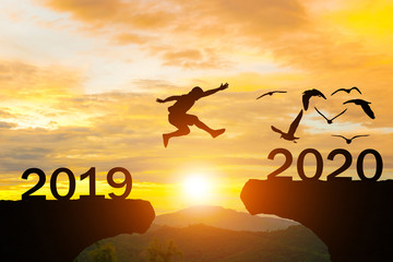 Happy New Year 2020 Men jump over silhouette mountains sun