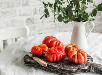 Heirloom ripe tomatoes on rustic cutting board to light the kitchen table on a light background