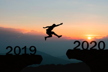 Happy New Year 2020 Men jump over silhouette mountains sun