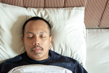 Top view of Asian man smiling while sleeping in his bed at home