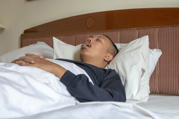 Tired Asian man sleeping with mouth open after work on a comfortable bed