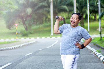 Asian young man with obesity confidently lifts a barbell and poses in front of the camera