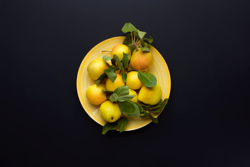 Ripe yellow pears with leaves on a yellow dish on a dark background.  Autumn flat lay composition. Top view.