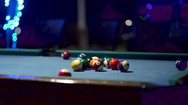 Panning shot of a billiard table with pool balls, with bar lights in the background