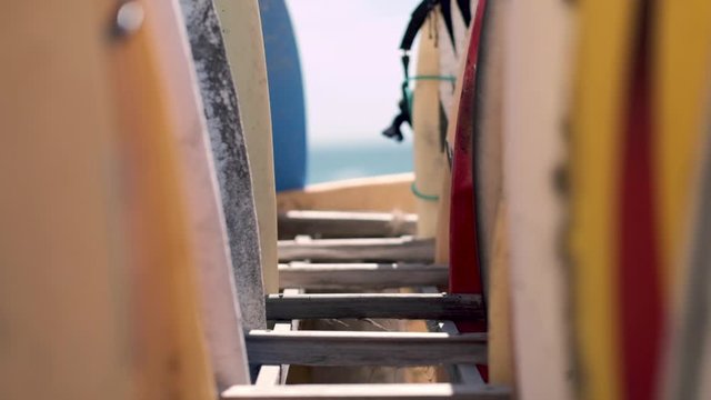 Close up, tilt shot, of many colorful surf boards in wooden racks, on a sandy beach