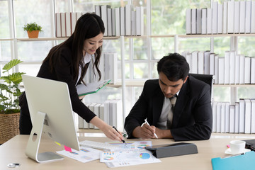 Two business people man and asian woman in black suit talking  planning business strategy. They pointing paperwork Marketing plan researching. Business teamwork, brainstorming concept
