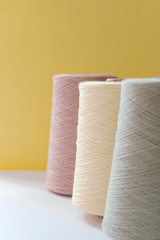 Pastel color bobbins of wool yarn for hand and machine knitting on a yellow background