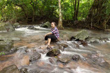 Fototapeta na wymiar Asian women be smile sitting relaxing and enjoying view in waterfall in greens jungle. Traveling along mountains and rain forest, freedom and active lifestyle concept. Asia, Thailand