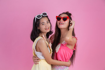 Two Asian girls who are friends are happy and have a pink background.