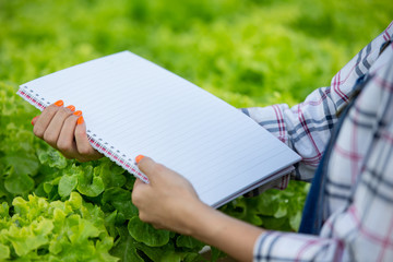 The girl's hand holding a white book on a green nature background.